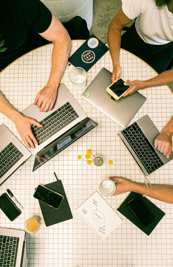 Top view of a team collaborating with laptops, phones, and notes in a modern office.