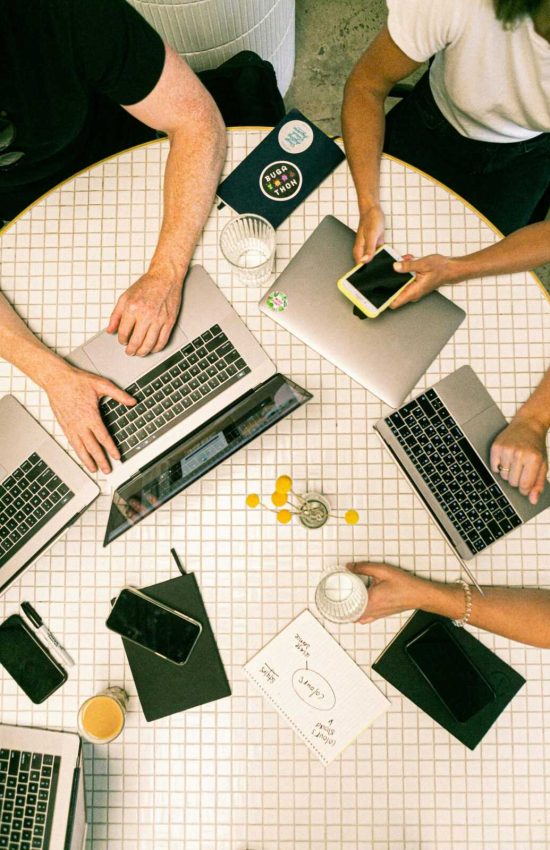 Top view of a team collaborating with laptops, phones, and notes in a modern office.