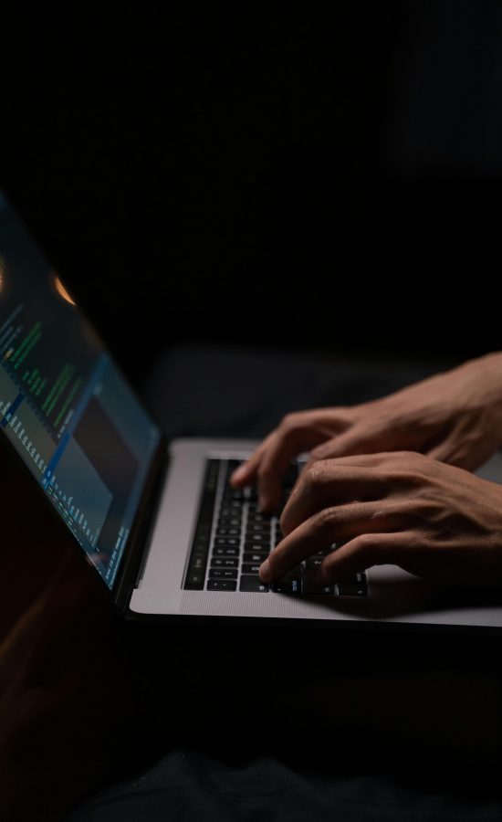 Hands typing code on a laptop keyboard in a dark room, capturing the essence of late-night programming.