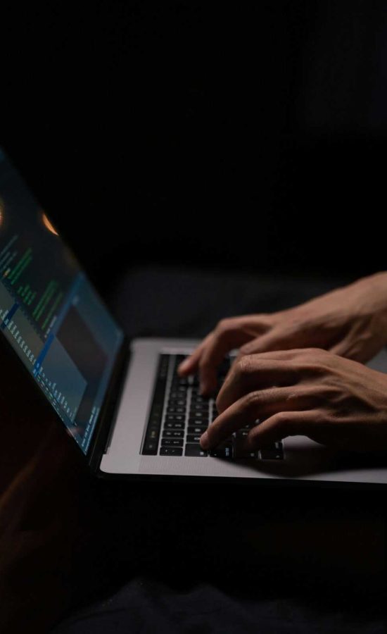 Hands typing code on a laptop keyboard in a dark room, capturing the essence of late-night programming.