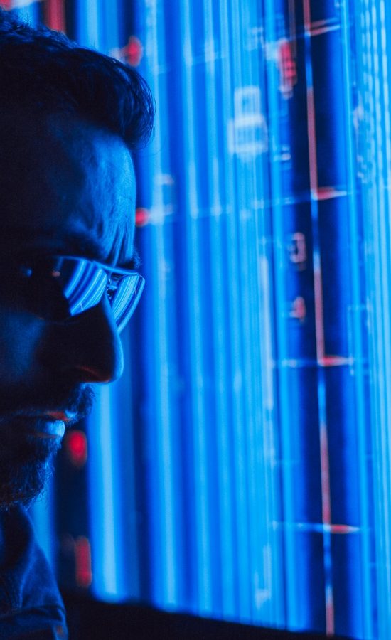 A man in sunglasses intently studies a vibrant blue holographic screen, symbolizing digital technology.